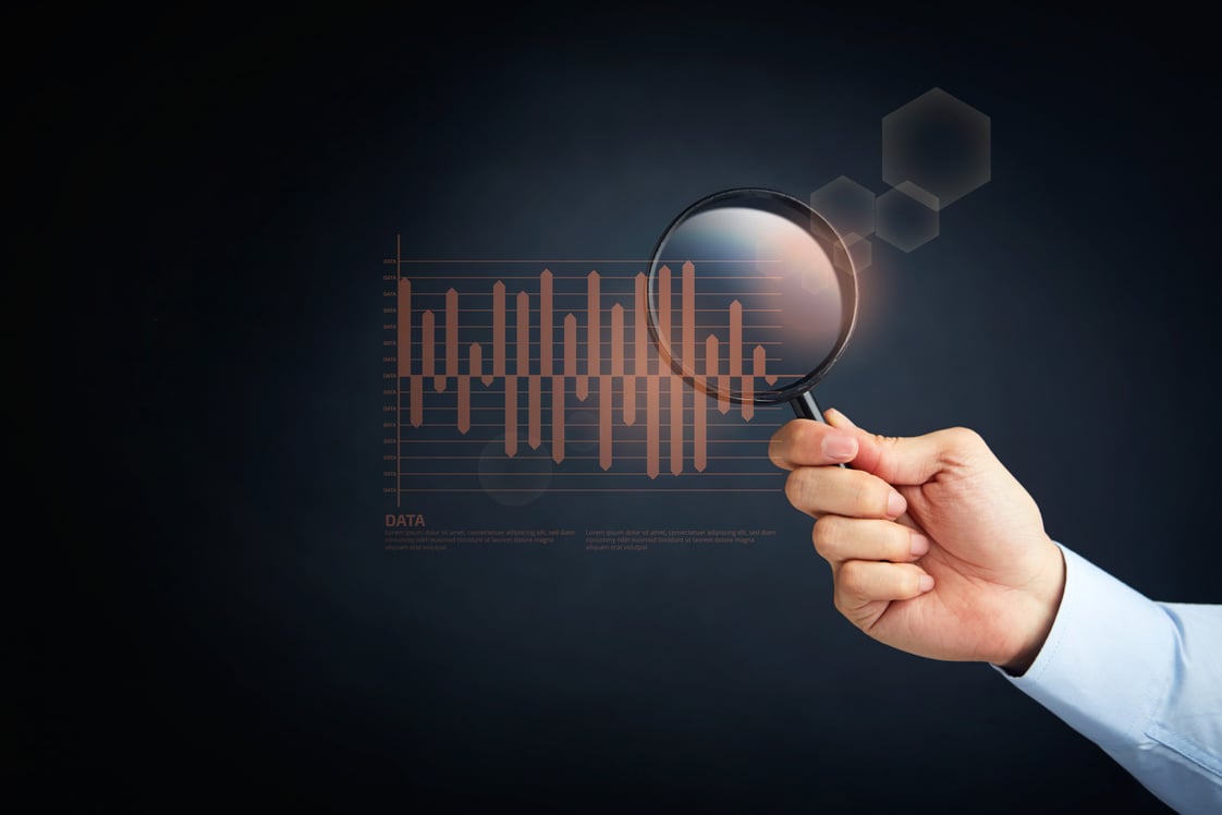 Hand holding a magnifying glass with statistics graph